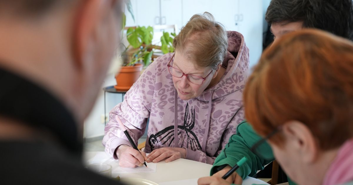 Henkilö kirjoittaa kynällä paperiin pöydän ääressä.