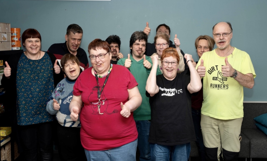 Ryhmäkuvassa iloisia ihmisiä, jotka näyttävät peukkuja.