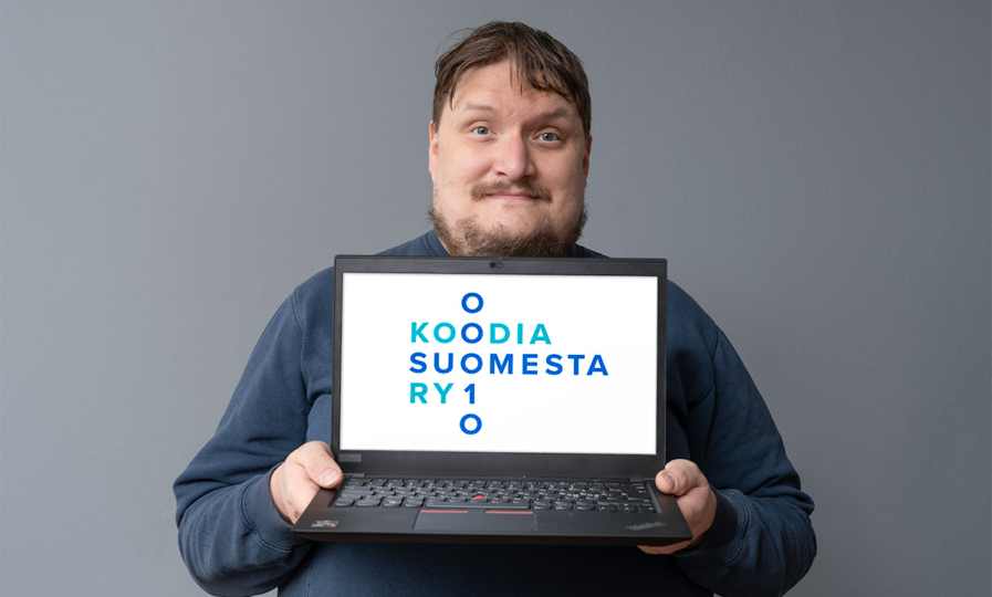 Henkilö pitää vartalonsa edessä kannettavaa tietokonetta, jonka näytöllä on Koodia Suomesta -logo.